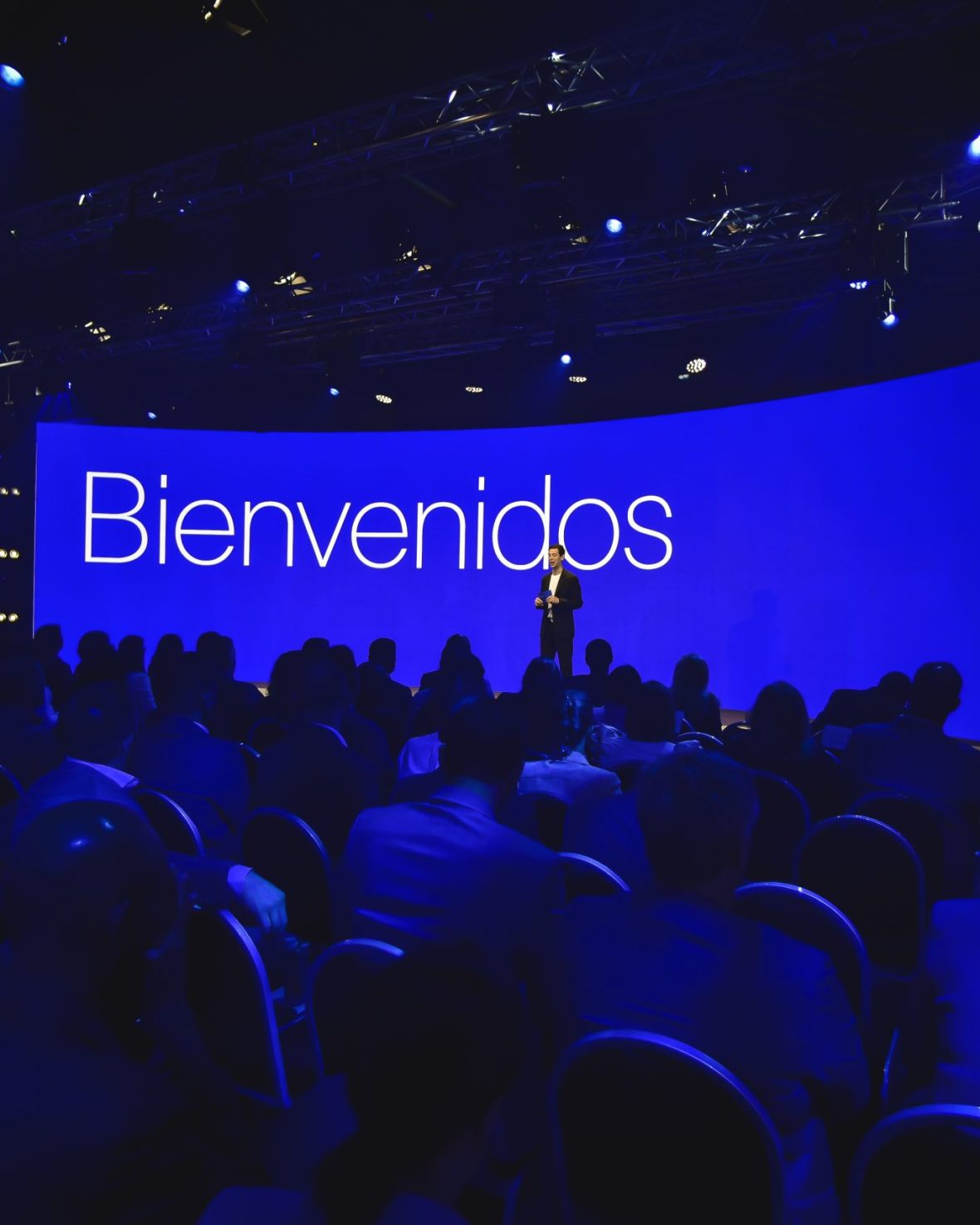 Speaker welcoming the audience on stage in front of a large blue screen reading “Bienvenidos” during the Conference in Buenos Aires – Immersive 360°.