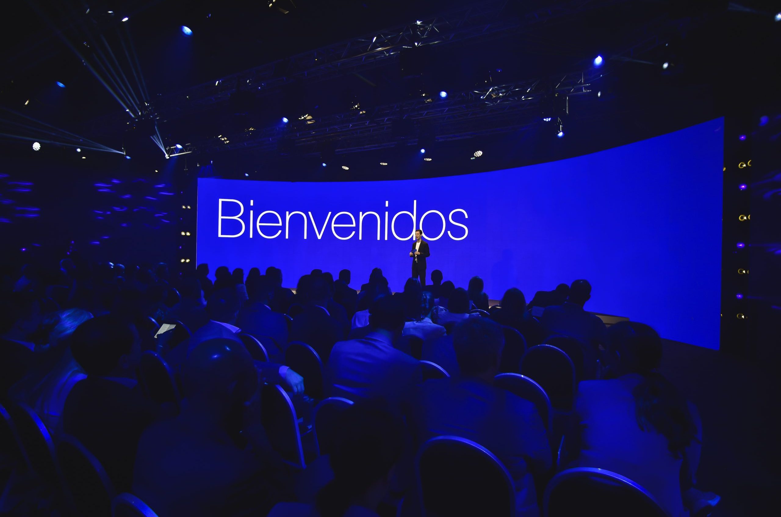 Speaker welcoming the audience on stage in front of a large blue screen reading “Bienvenidos” during the Conference in Buenos Aires – Immersive 360°.