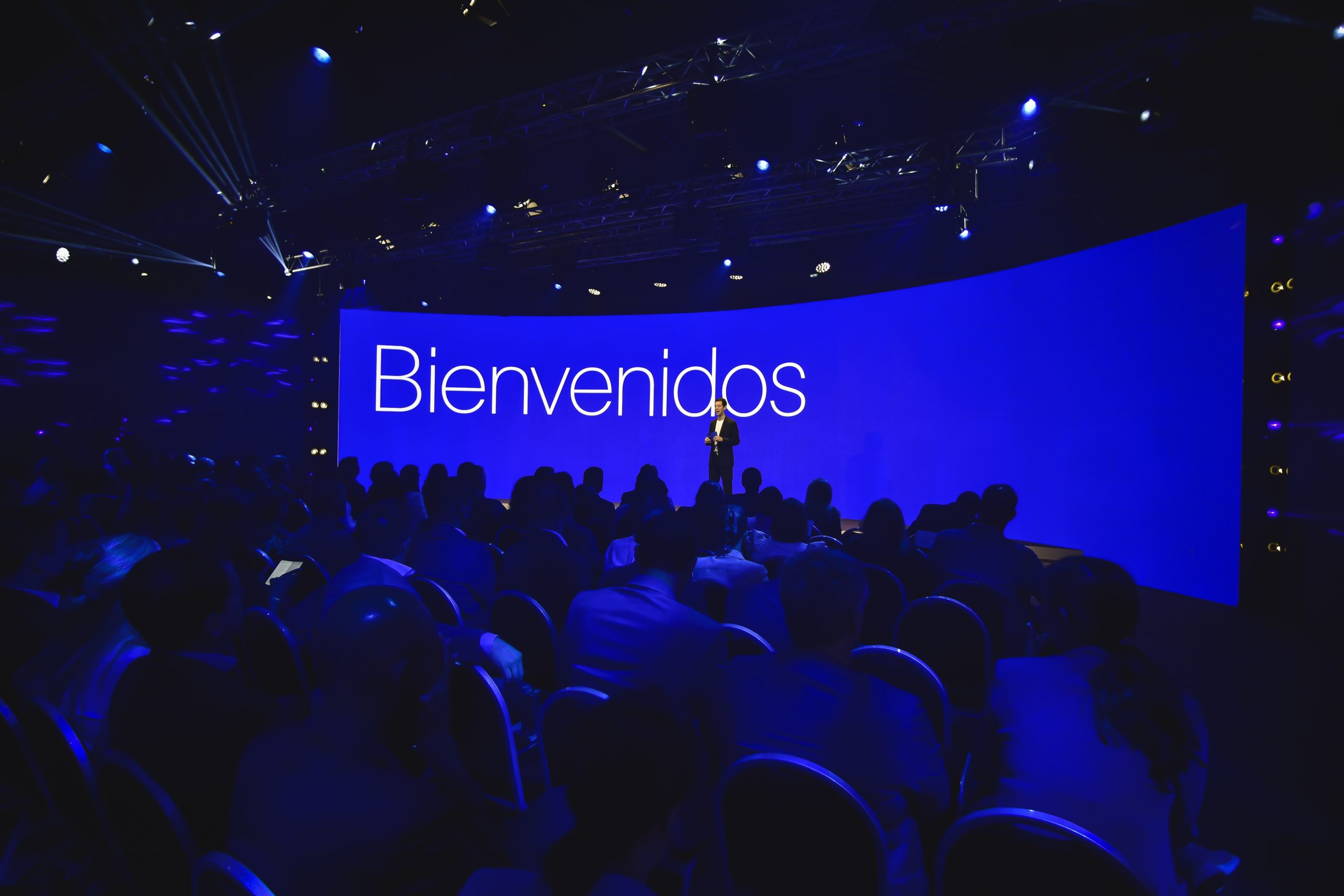 Speaker welcoming the audience on stage in front of a large blue screen reading “Bienvenidos” during the Conference in Buenos Aires – Immersive 360°.