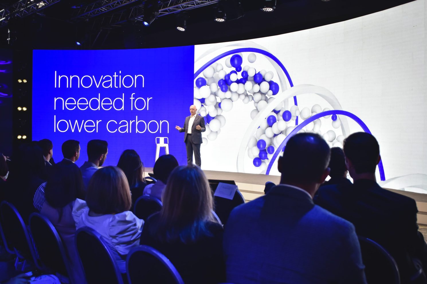 Speaker presenting on stage in front of a large immersive screen reading “Innovation needed for lower carbon” during the Conference in Buenos Aires – Immersive 360°.