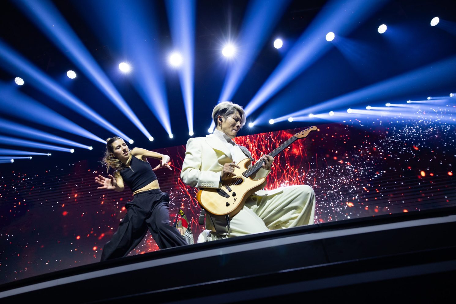 Guitarist performing on stage alongside a dancer during the Nansen Refugee Award – Hybrid Ceremony, with dynamic lighting and a large illuminated screen in the background.