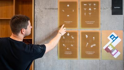 Man interacting with an interactive wall display during the MEA – Opening of MEA at Geneva, pointing at illustrated panels mounted on a concrete wall inside an exhibition space.