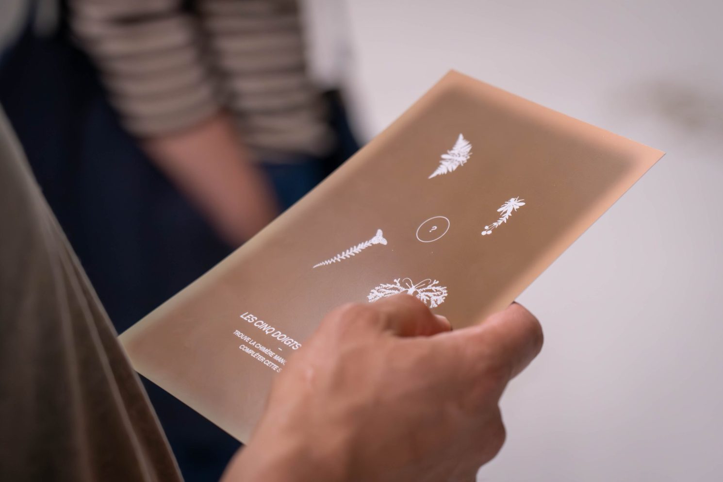 Hand holding a translucent panel with white botanical illustrations and printed text during the MEA – Opening of MEA at Geneva.