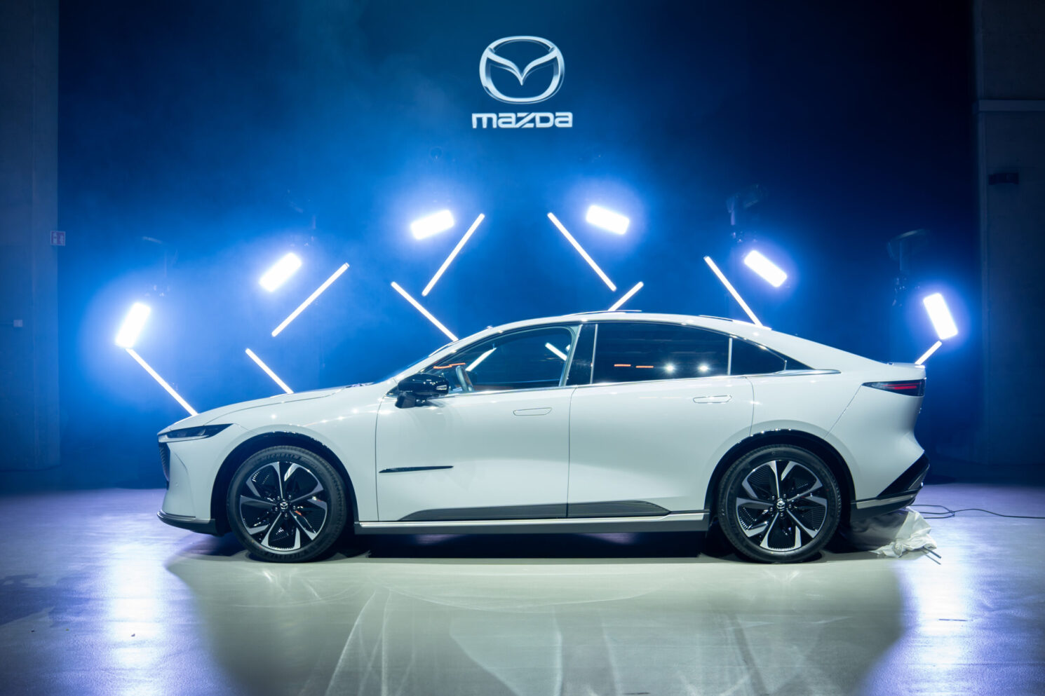 Mazda 6E unveiled on stage in a cinematic lighting setup with the Mazda logo displayed above during the Mazda – Cinematic reveal of the Mazda 6E.