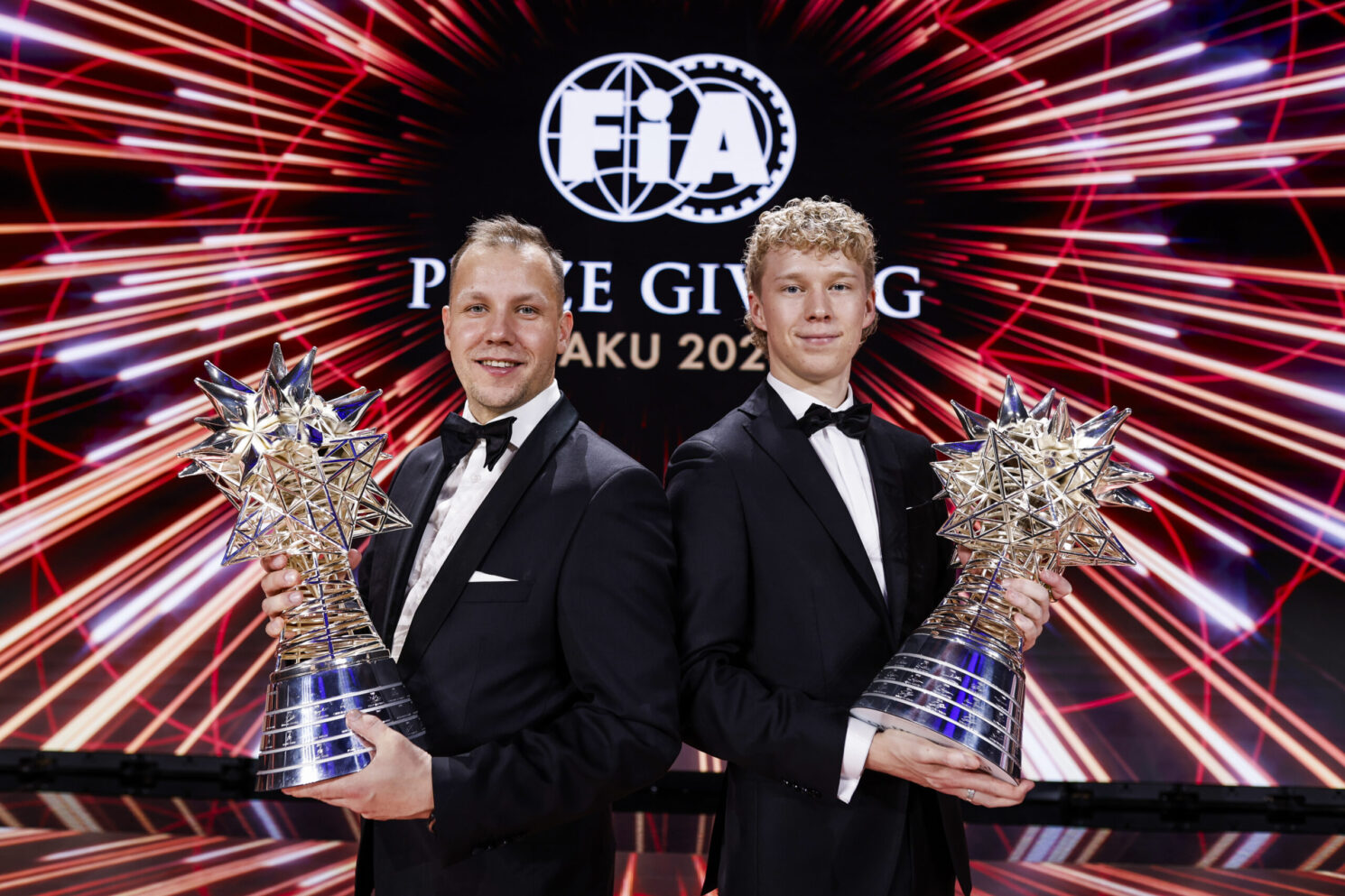Two award winners holding trophies on stage during the FIA – Motorsport Award Ceremony, standing in front of a dynamic “FIA Prize Giving Baku 2023” backdrop.